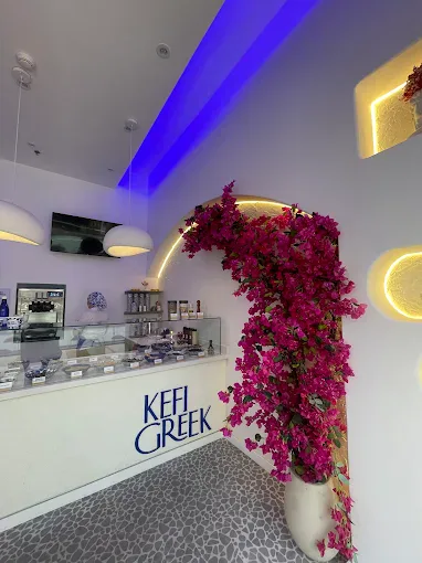 Mostrador de Kefi Greek con el letrero azul y un arco cubierto de buganvilias